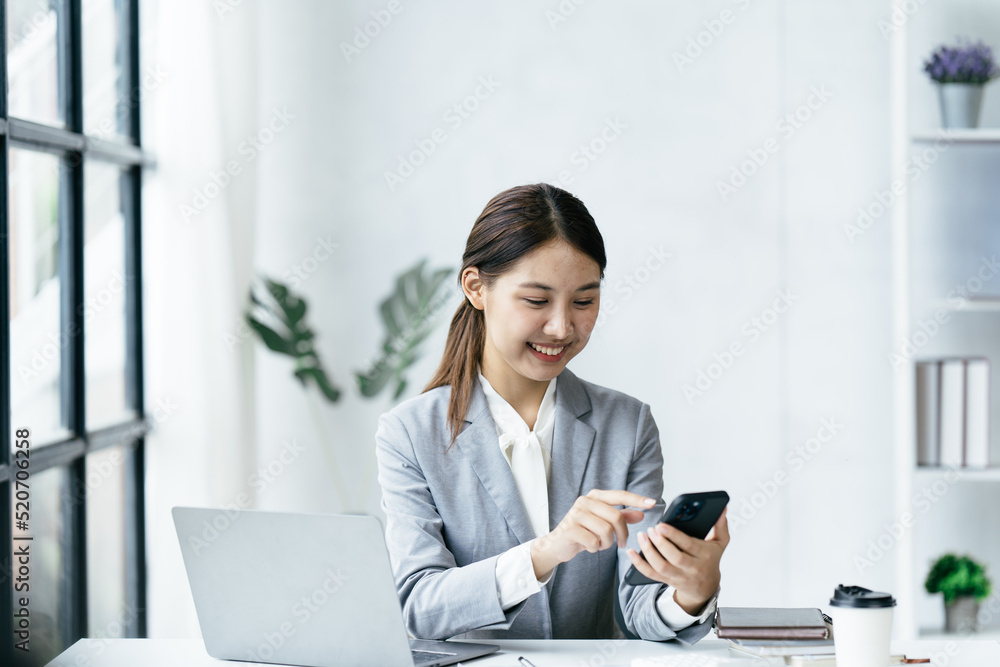 Asian businesswoman in formal suit in office happy and cheerful during using smartphone and working.