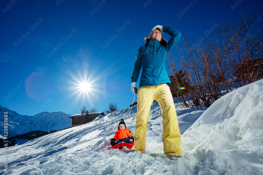 冬天雪地里，妈妈和小男孩在山上拉雪橇