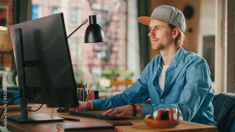 Young Handsome Adult Man Wearing a Cap, Working from Loft Apartment on Desktop Computer. Talented Ma