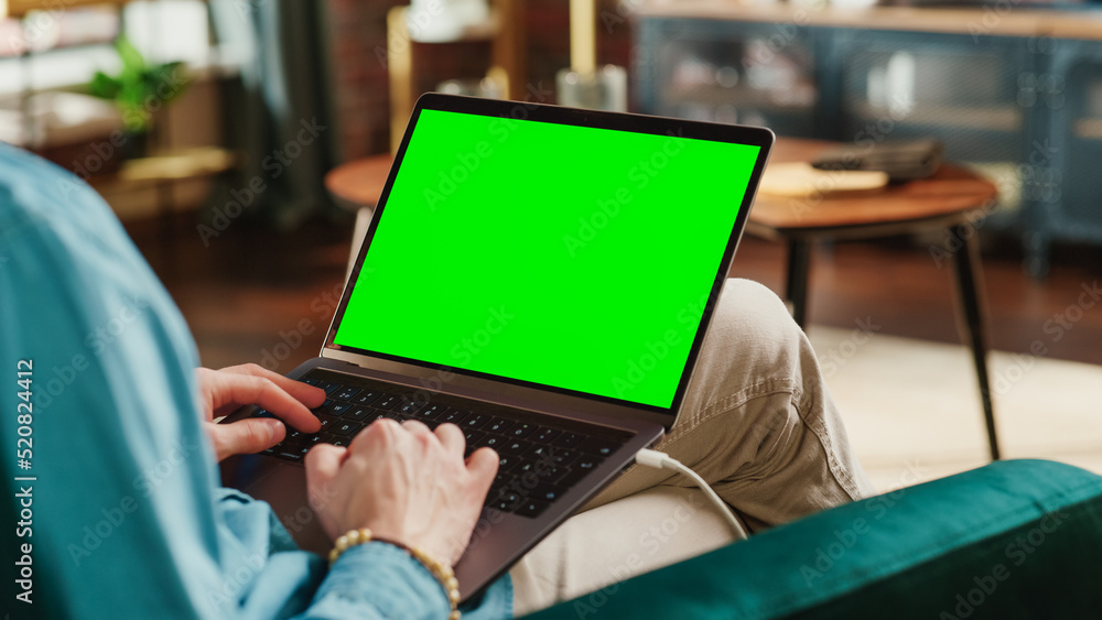 Young Adult Man Working from Home Loft Apartment on Laptop Computer with Green Screen Mock Up Displa