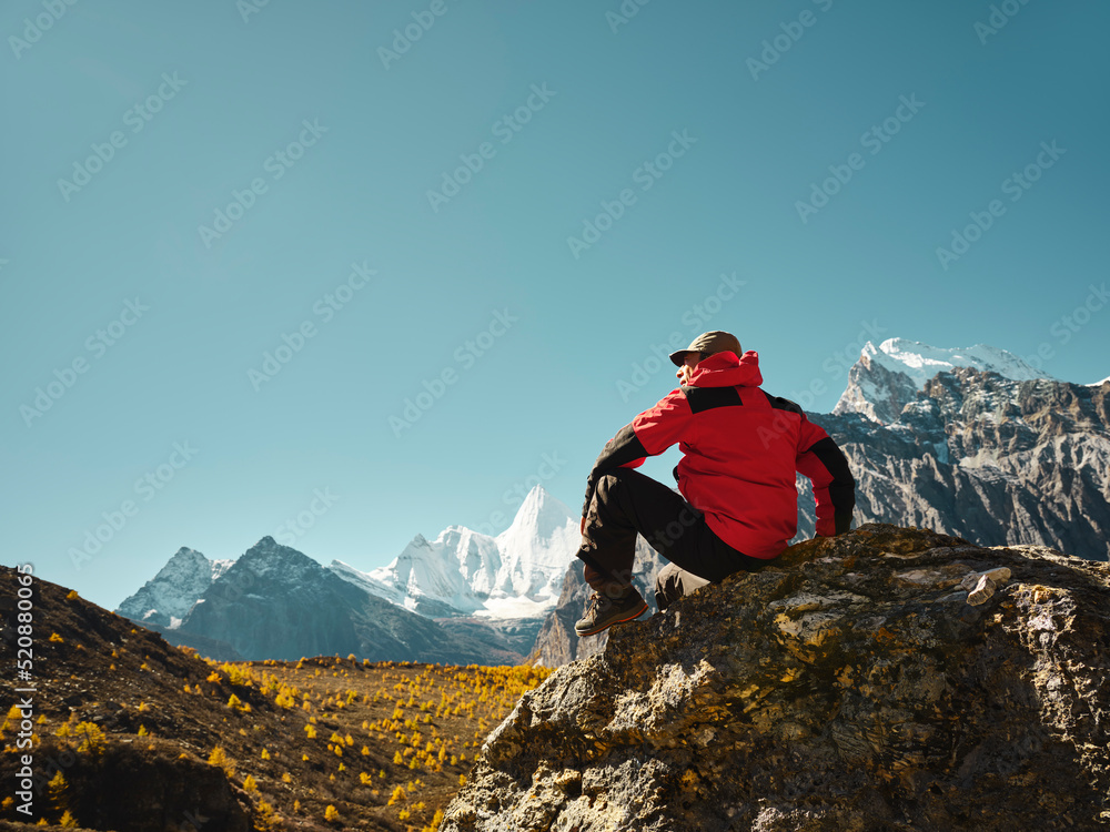 一名亚洲男子坐在岩石顶上，眺望西藏的羊迈雍山