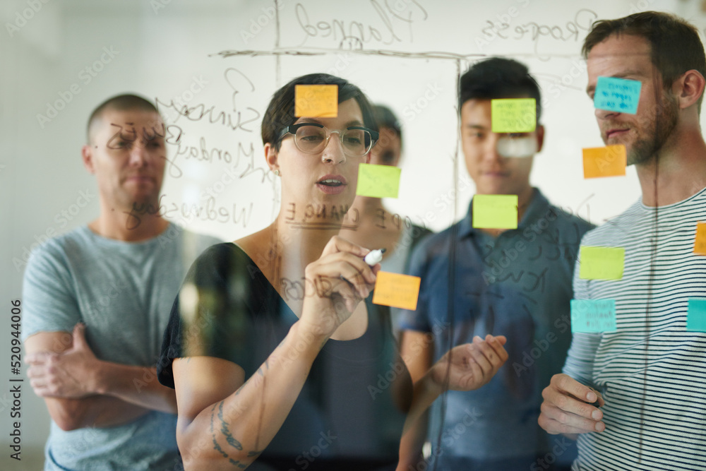 Designers planning a strategy for a group project on a glass whiteboard together in a meeting. Creat