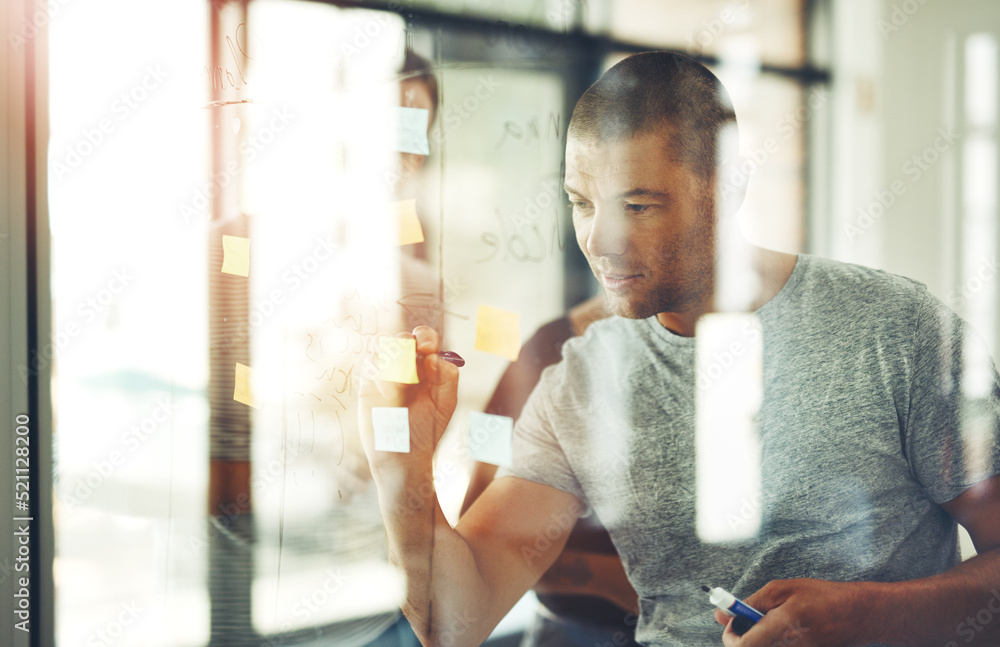 I have a clear vision of what I want. Shot of a man writing ideas on sticky notes with his team behi