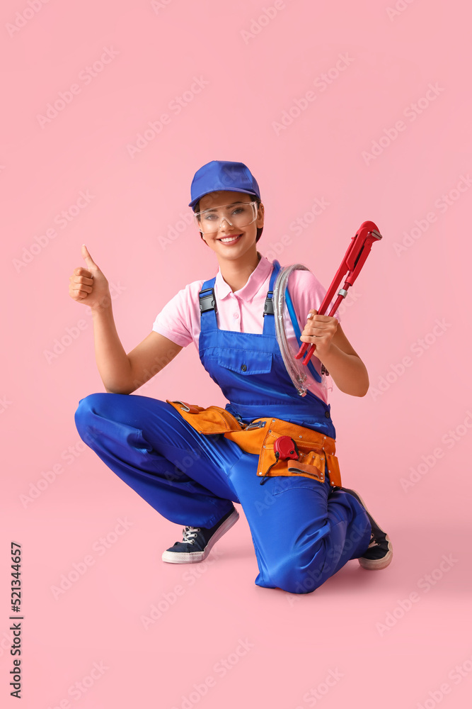 Female plumber with pipe wrench showing thumb-up on pink background