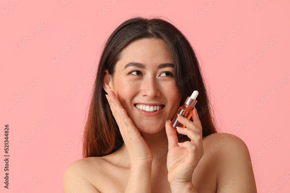 Young Asian woman with cosmetic serum on pink background