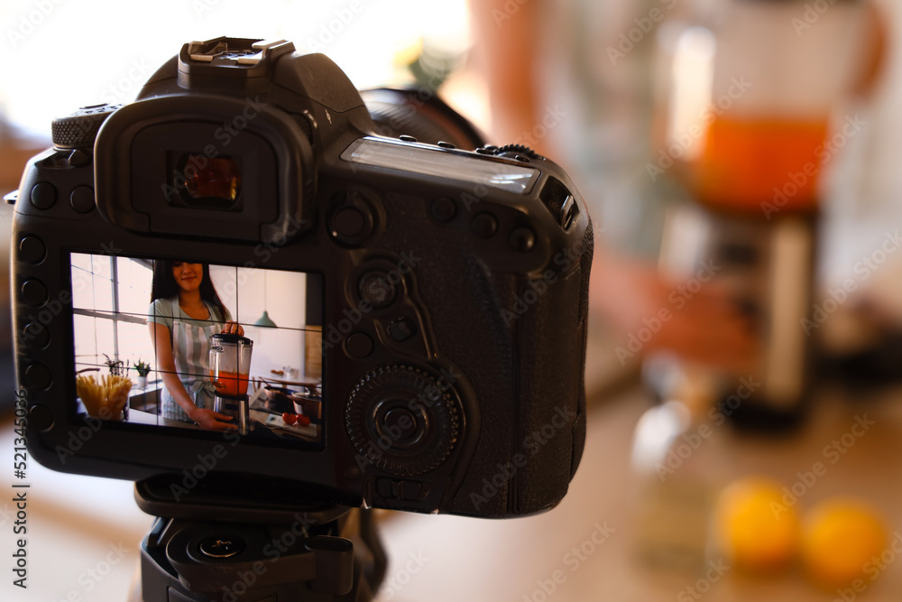 Young woman using blender on display of photo camera in kitchen, closeup