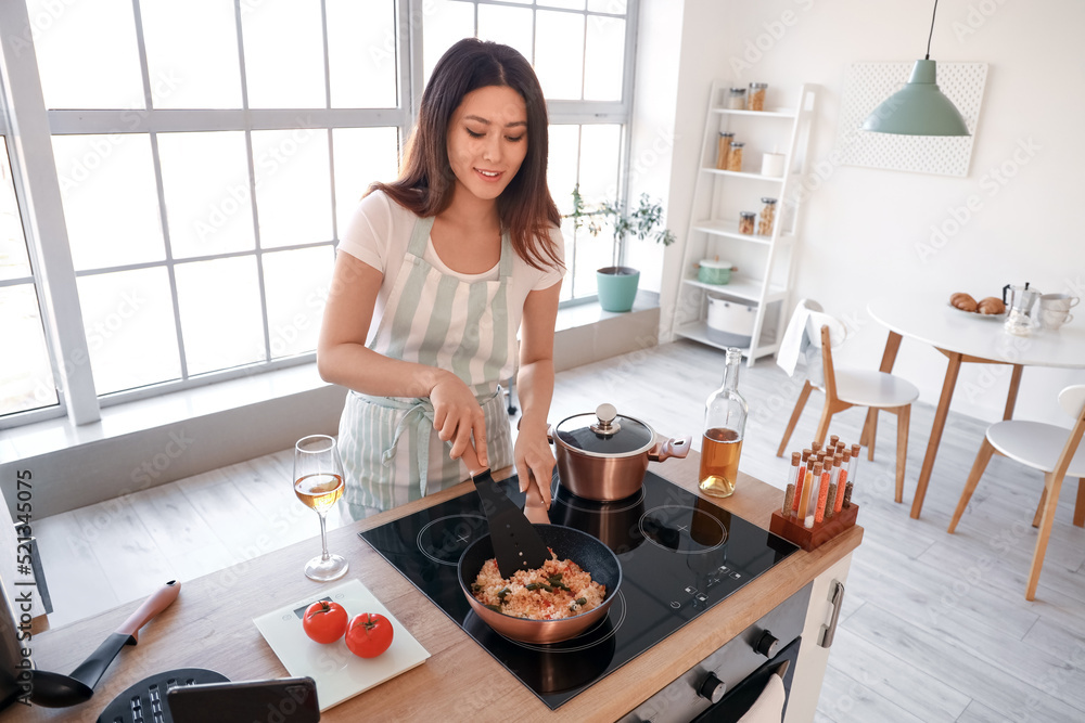 年轻的亚洲女人在厨房里一边跟着烹饪视频教程一边炒菜米饭