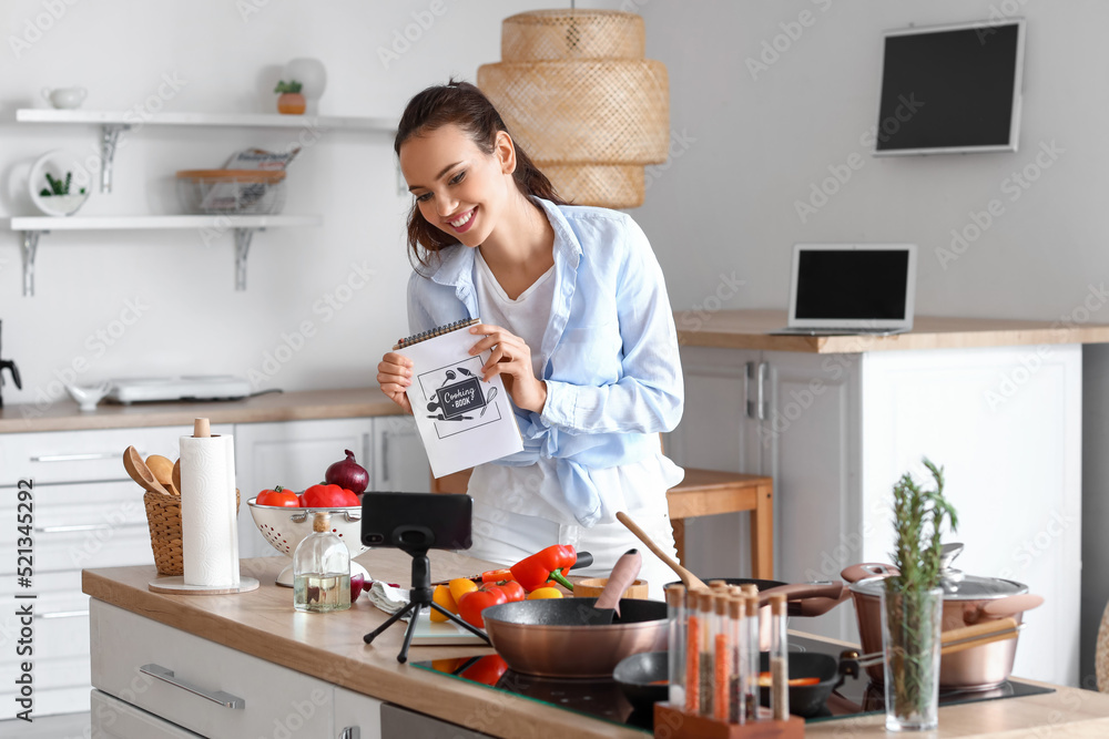 年轻女人带着烹饪书在厨房录制视频教程