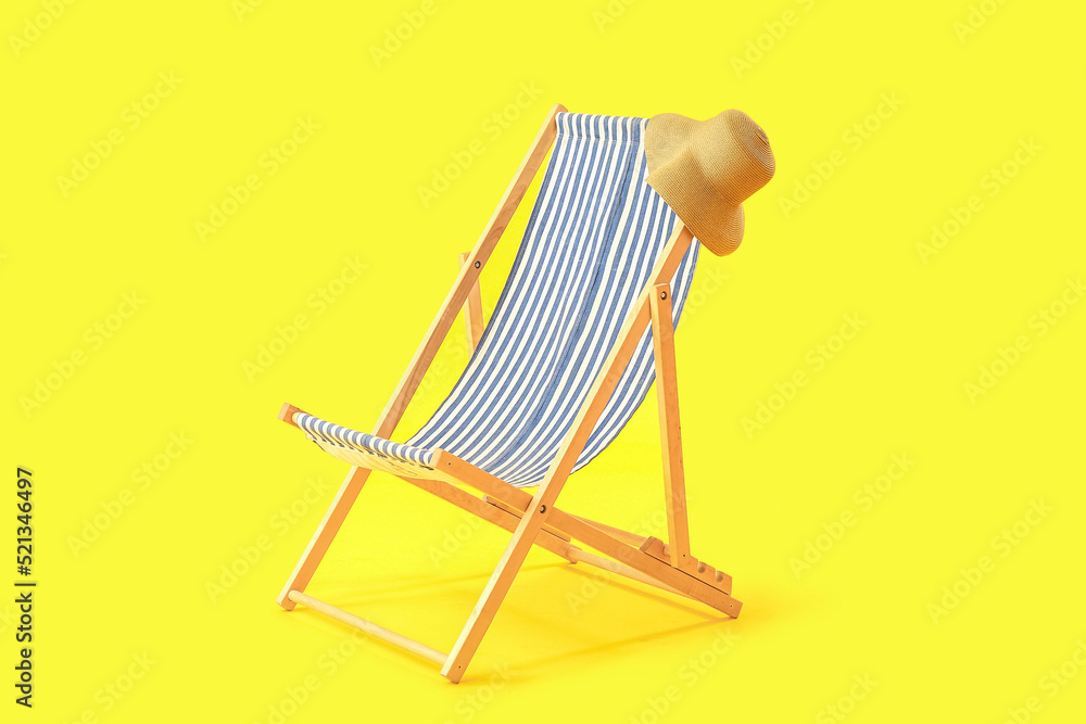 Wooden deck chair with hat on yellow background