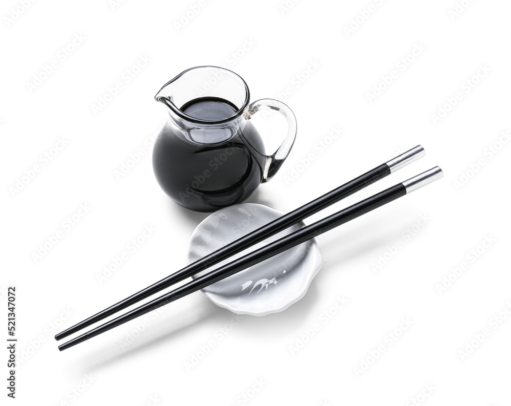 Jug of soy sauce and chopsticks on white background