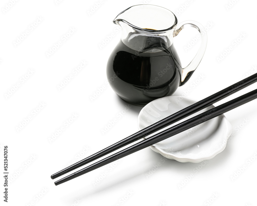 Jug of soy sauce and chopsticks on white background