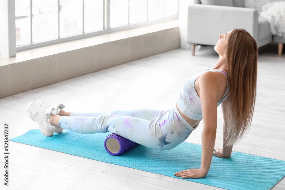 Young woman training with foam roller at home