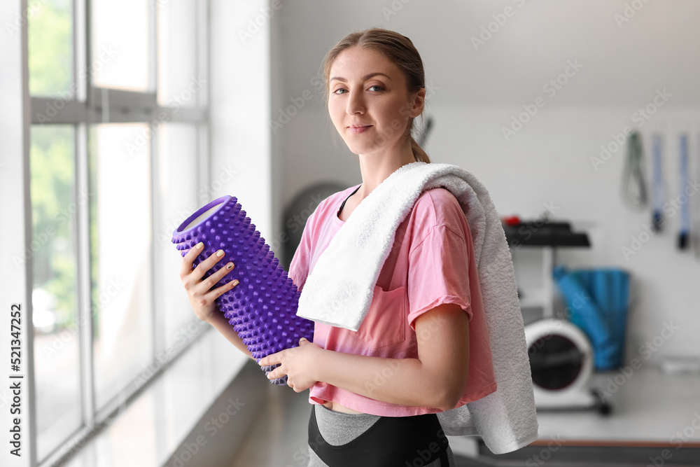 Young woman with foam roller and towel in gym