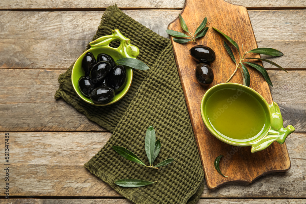 Composition with bowls of oil and olives on wooden background