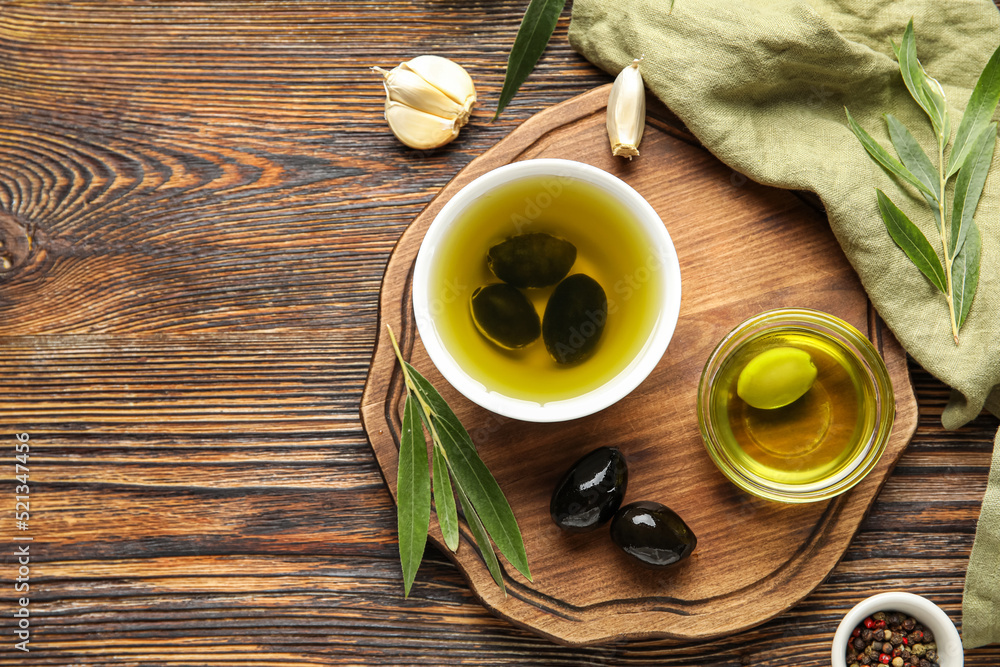 Composition with bowls of oil and olives on wooden background