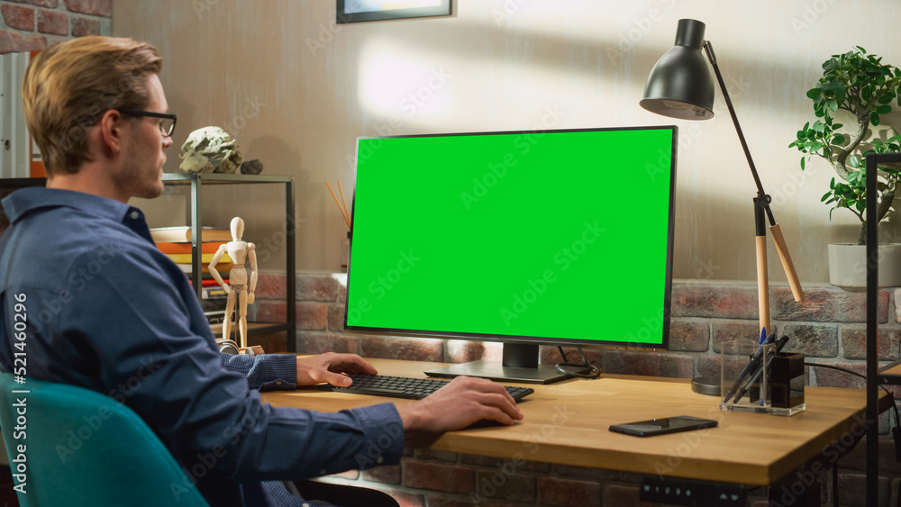 Young Handsome Man Working from Home on Desktop Computer with Green Screen Mock Up Display. Creative