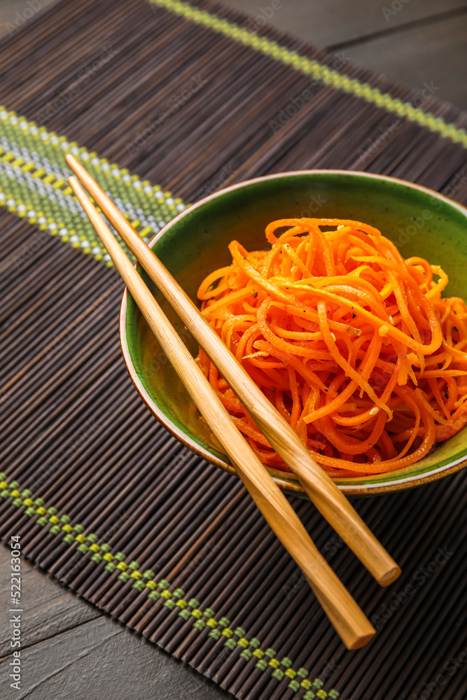 Bowl with carrot salad and wooden chopsticks on bamboo mat, closeup