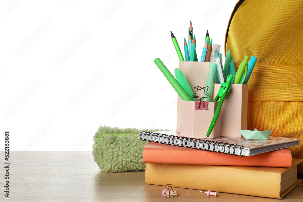 Cups with school stationery, pencil case and backpack on table against white background