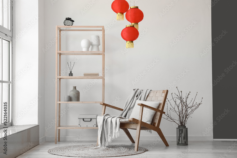 Interior of light living room with shelving unit, armchair and Chinese lanterns