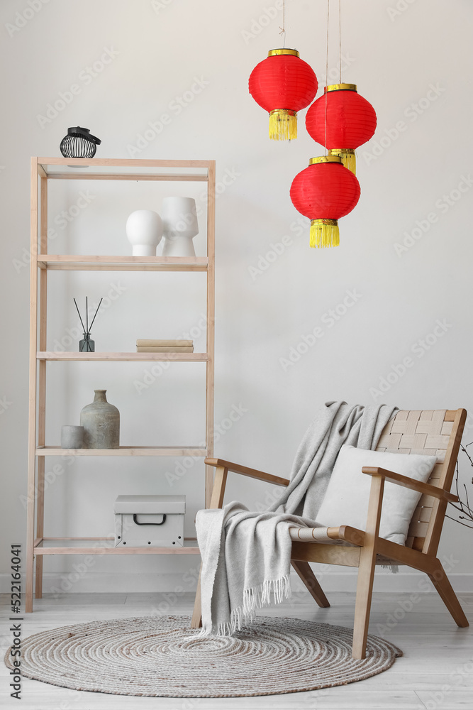 Interior of light living room with shelving unit, armchair and Chinese lanterns