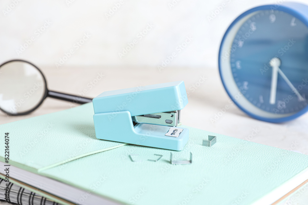 Stapler with stationery supplies and alarm clock on light background, closeup