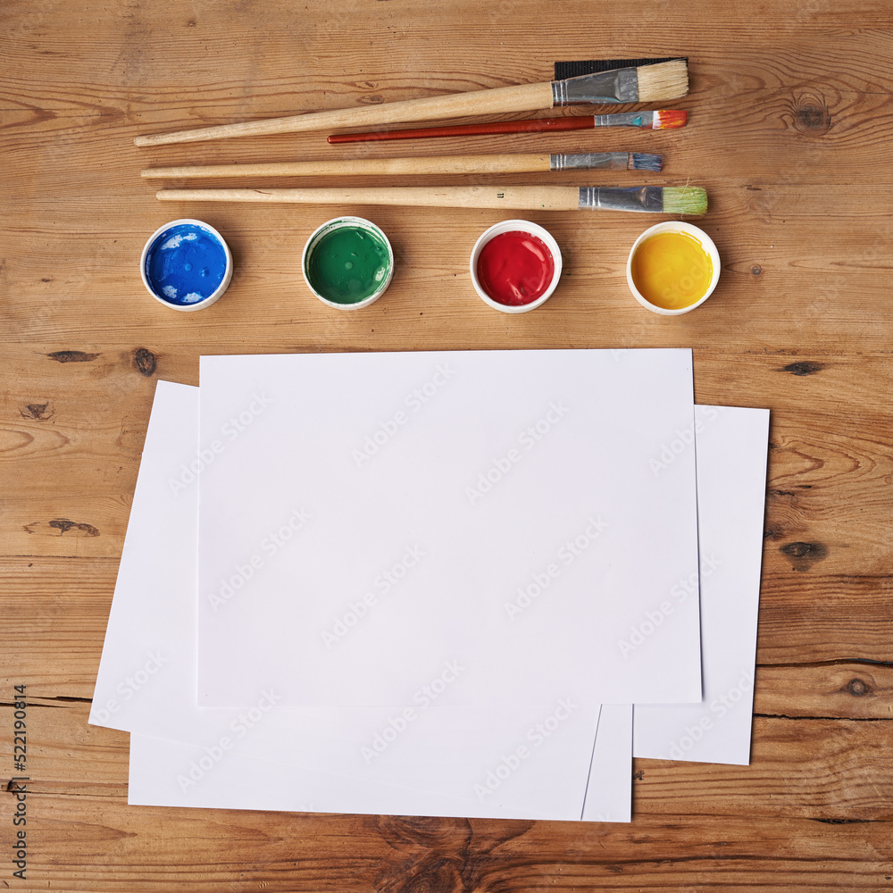 Art, painting and creative supplies on a wooden desk with paper from above. Paintbrushes, colors and