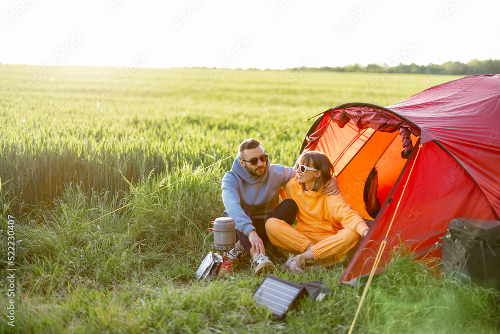 一对年轻夫妇在绿地帐篷附近的露营地共度夏天。充电小工具