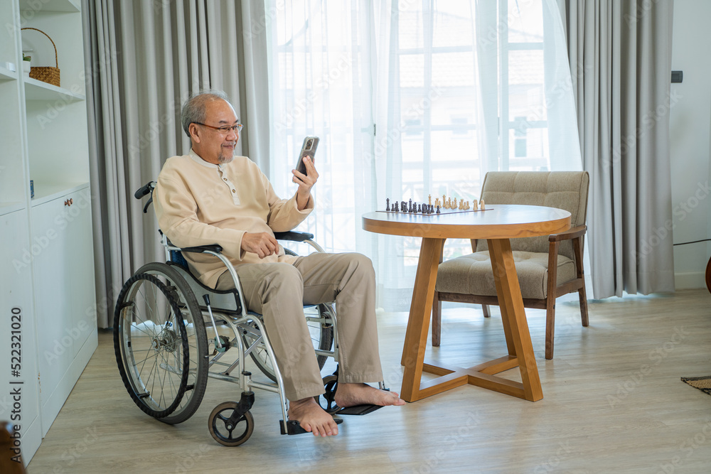 Senior man sitting on wheelchair and talking to relatives on video call conference in living room,Fa