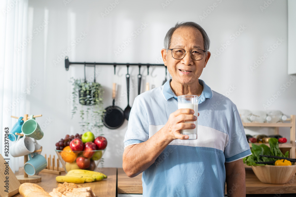 亚洲成年男子在家里的厨房里喝着一杯牛奶。