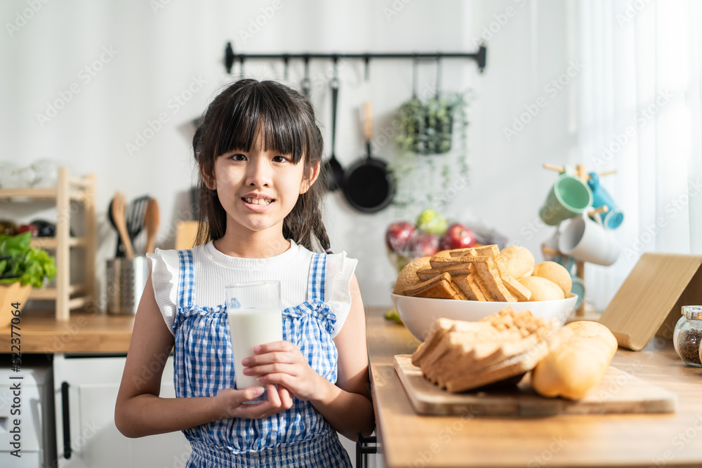 亚洲小孩拿着一杯牛奶在家里的厨房里喝水