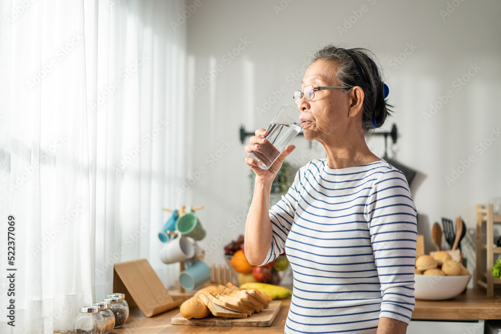 亚洲资深成熟女性在家里的厨房里喝着一杯牛奶。