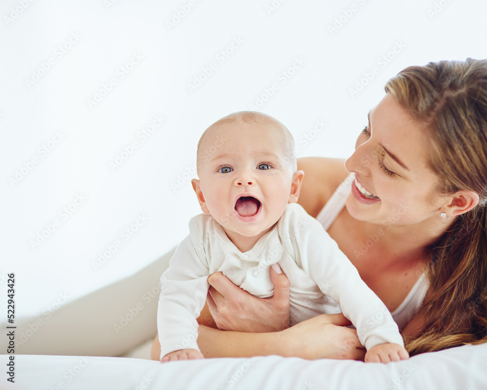 Loving mother and baby bonding at home, playing while relaxing on a bed together. Happy parent being