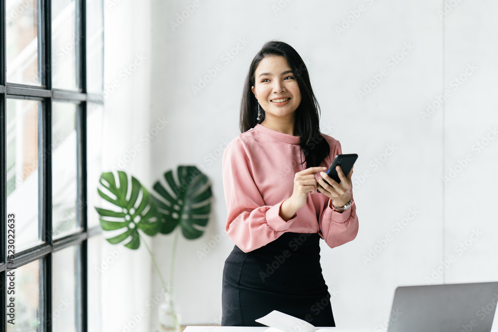 穿着正式西装在办公室的亚洲女商人，在使用智能手机和工作时心情愉快。