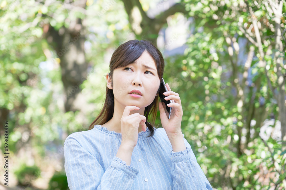 外で困りながらスマホで電話する女性