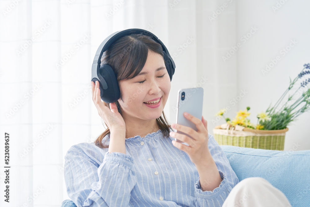 自宅でヘッドホンをしてスマホで音楽を聴く女性　