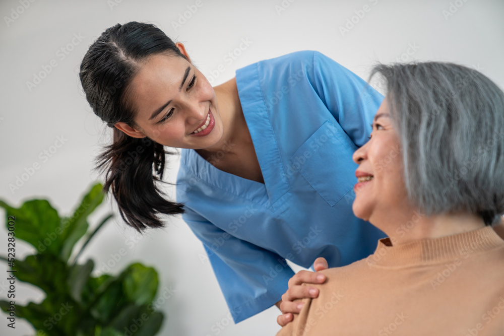 A caregiver rest her hands on the shoulders of a contented senior patient while she sitting on the s