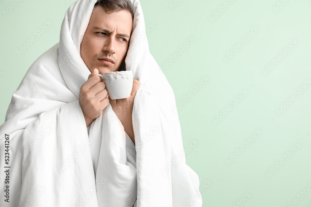 Sleepy young man with blanket and cup of coffee on green background