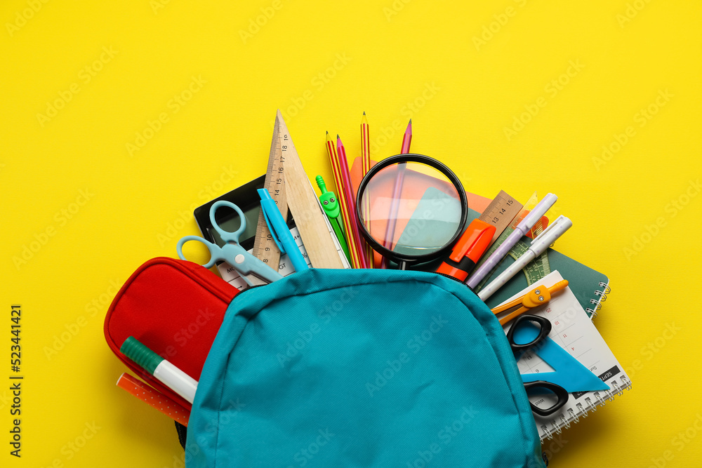 School backpack with stationery supplies on yellow background