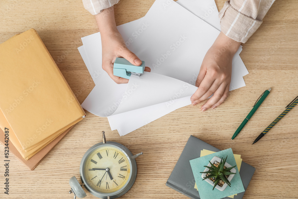 Woman with stapler, paper sheets, books and alarm clock at wooden table