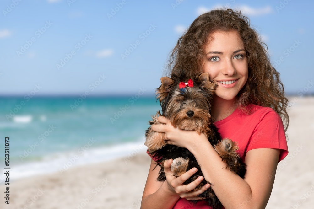 年轻女子在海滩上拥抱小狗，在旅行和度假时很开心。雌性与宠物一起开心地微笑