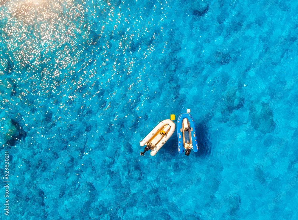 Aerial view of the boats in clear blue water at sunset in summer. Top view from drone of yachts, san