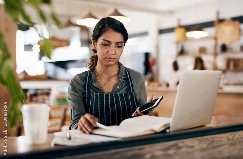 Cafe owner with laptop, phone and book checking online order, searching available bookings and prepa