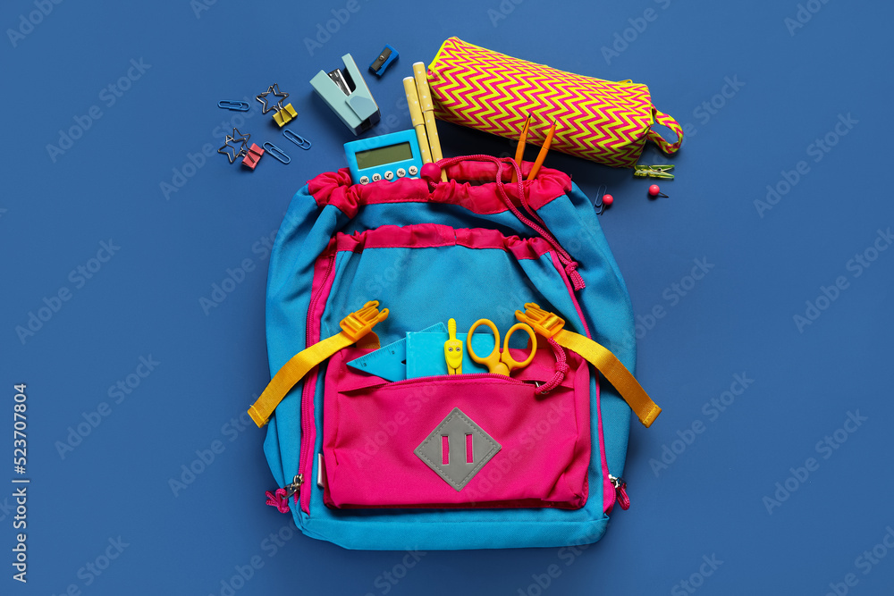 School backpack with stationery on blue background