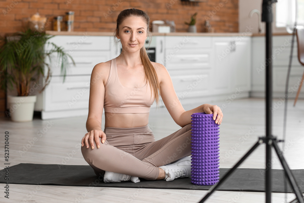 Young woman with foam roller recording video in kitchen