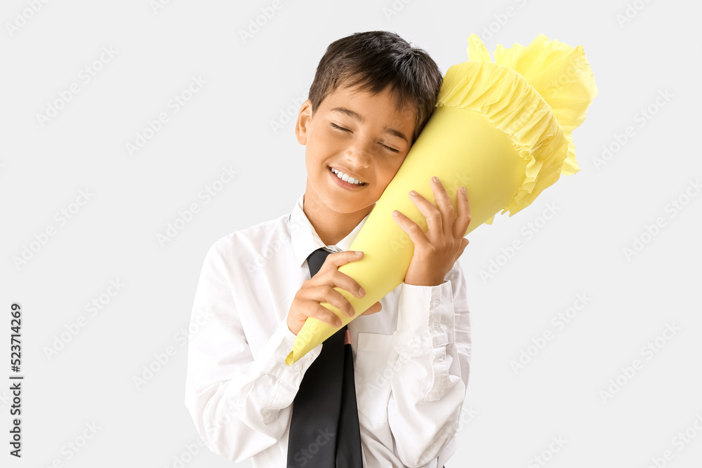 Happy little boy with yellow school cone on light background