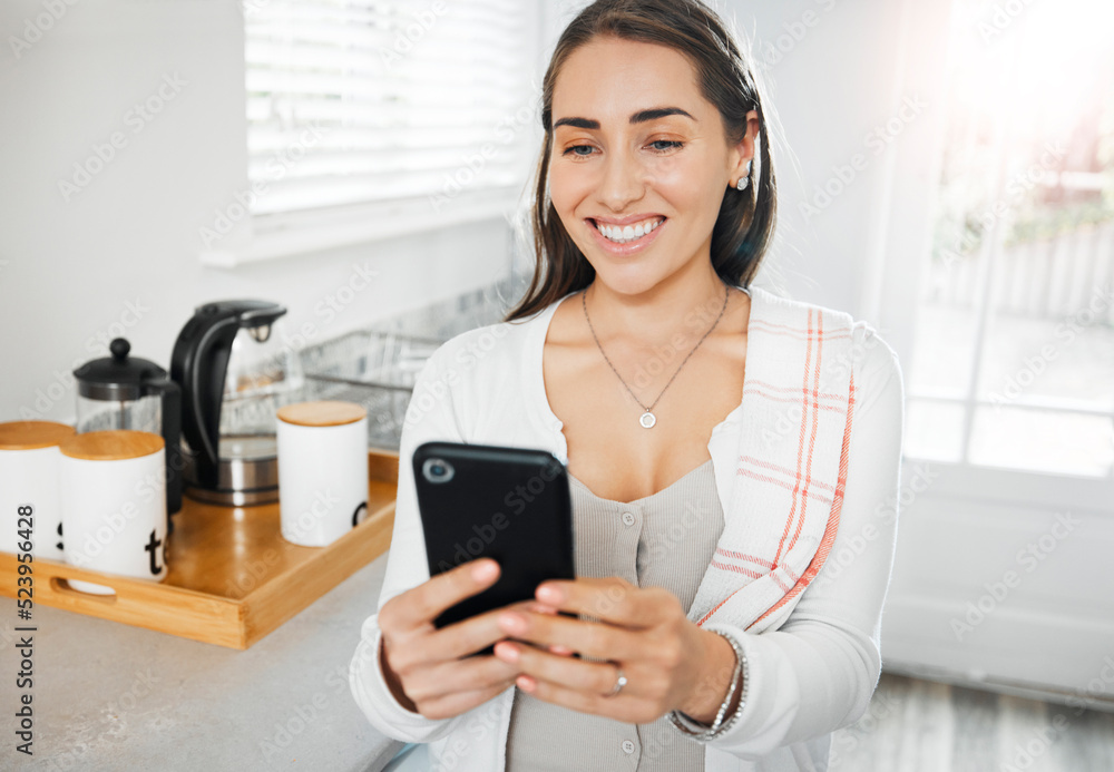 Woman browsing, texting and reading on a phone in her kitchen at home. Smiling woman on social media