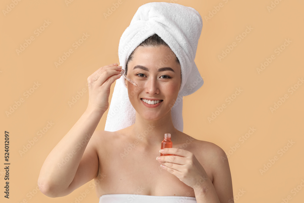 Young Asian woman with cosmetic serum on beige background