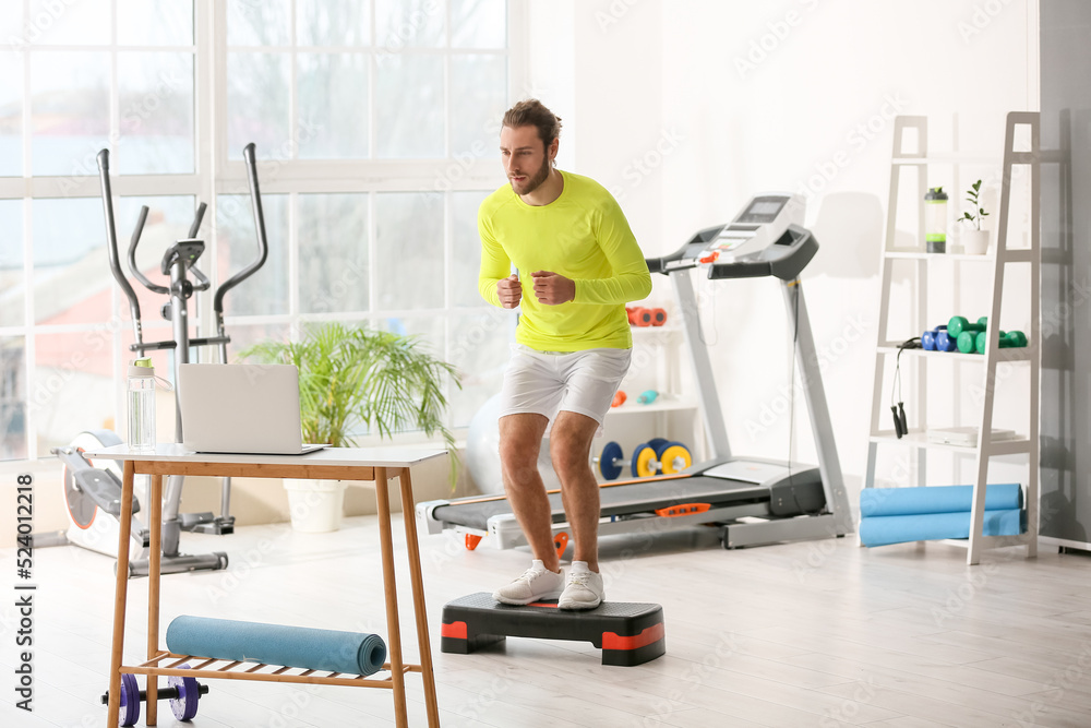 Sporty young man using laptop for online training in gym