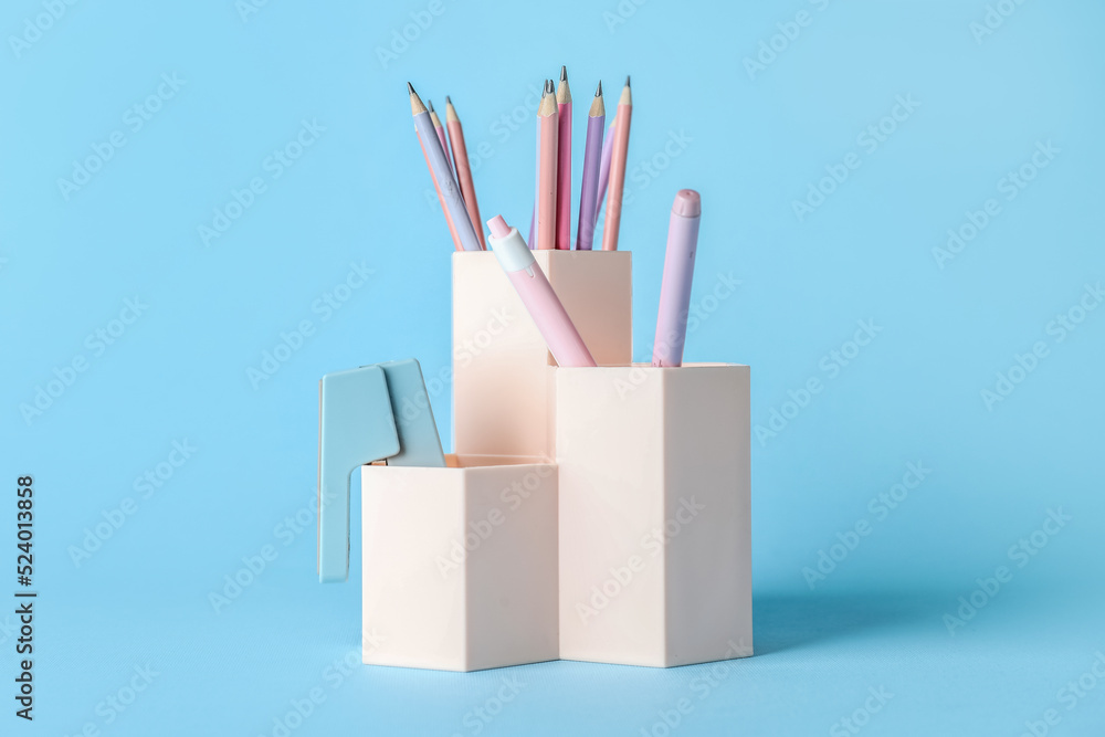 Cups with pens, pencils and stapler on blue background