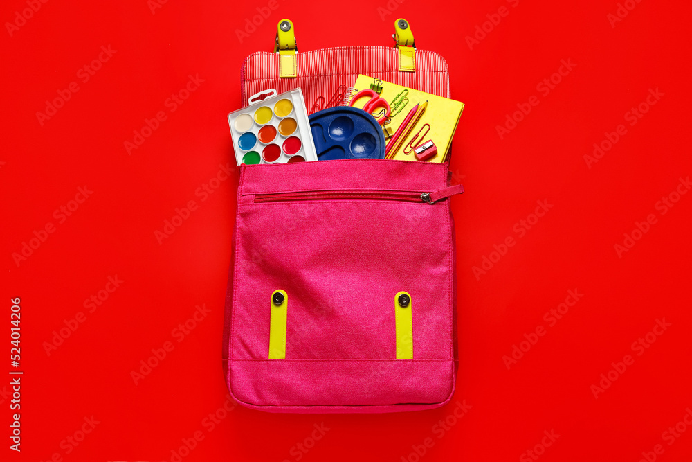 Pink backpack with school stationery on red background